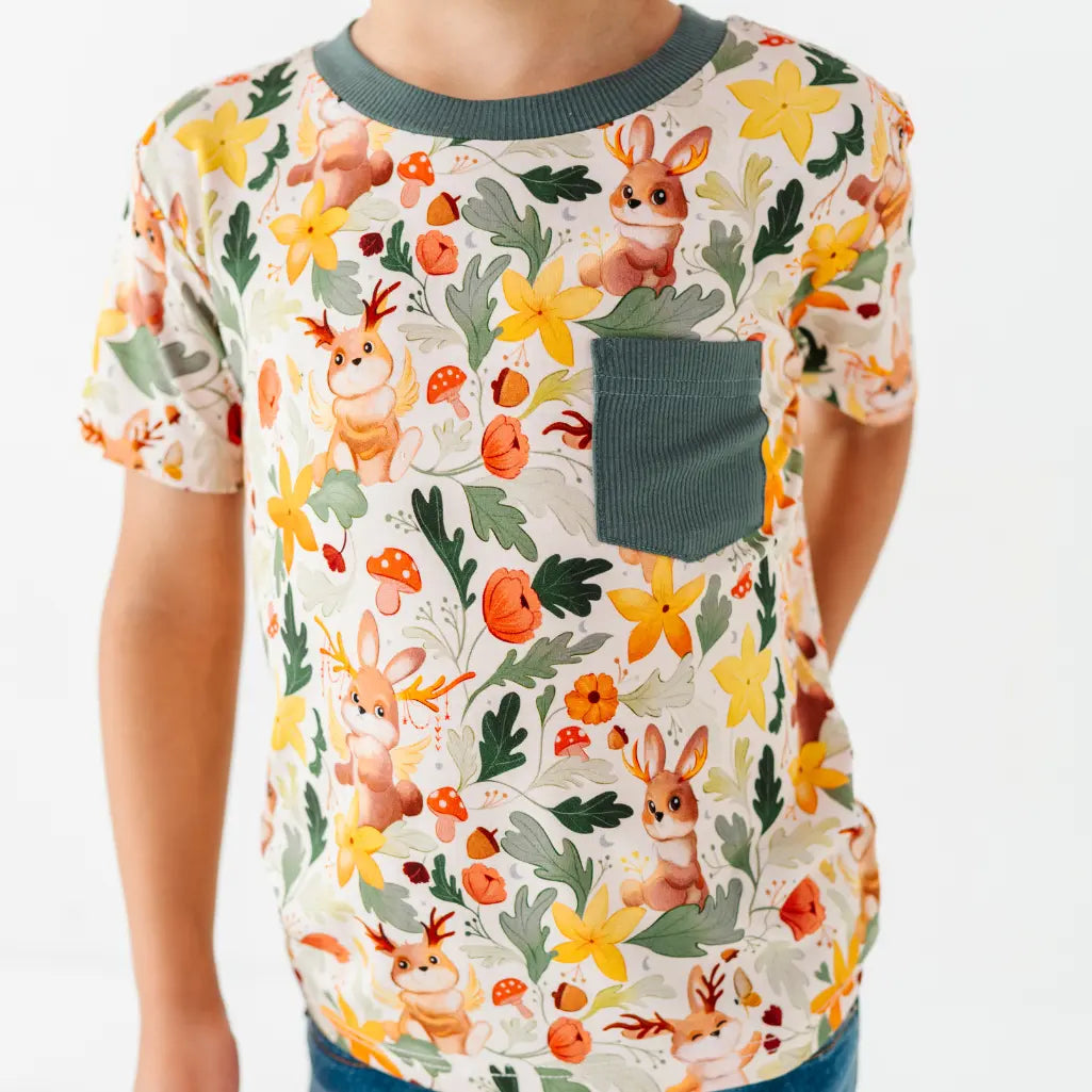 A cropped view of a child in a woodland print pocket tee with a dark green chest pocket and collar.
