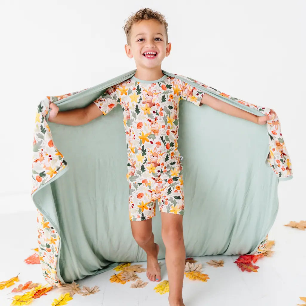A child holding a large blanket open like a cape, sage green on one side and woodland jackalope print on the other.