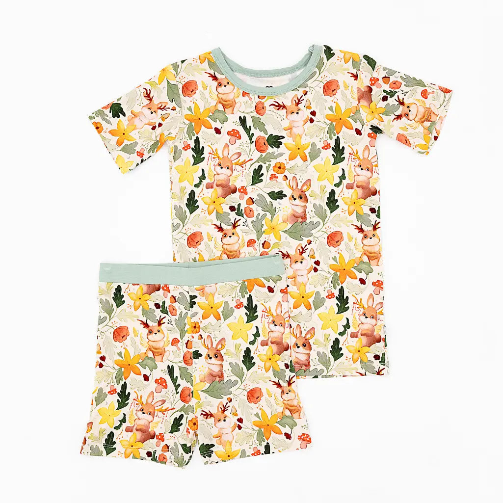 A short sleeve pajama top and matching shorts with sage green trim laid flat on a white background in a woodland jackalope print.