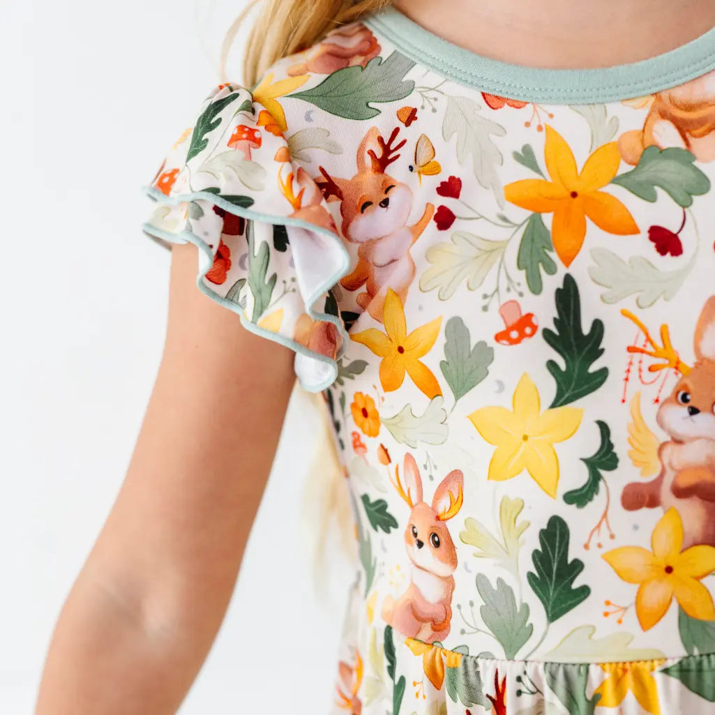 A close up of a child wearing a flutter sleeve dress with sage trim printed with antlered bunnies and yellow flowers.