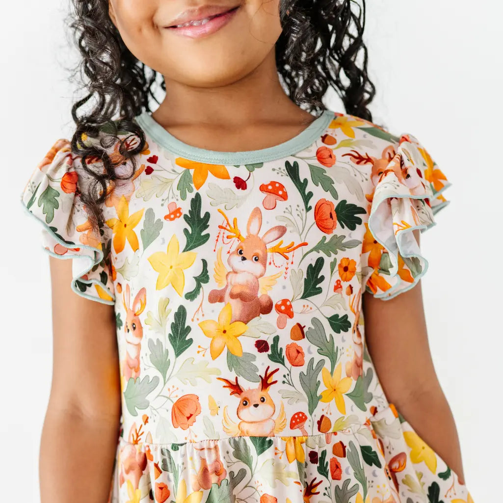 A close up of the flutter sleeves and bodice of a woodland jackalope print dress worn by a child.