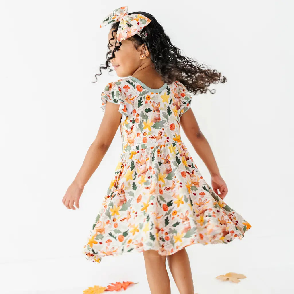 A child twirling in a woodland jackalope print dress with a matching bow headband as leaves lie on the floor.
