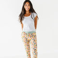 An adult standing on a white backdrop in woodland print pajama pants with a sage waistband and a white tee.