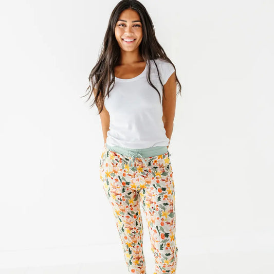 An adult standing on a white backdrop in woodland print pajama pants with a sage waistband and a white tee.