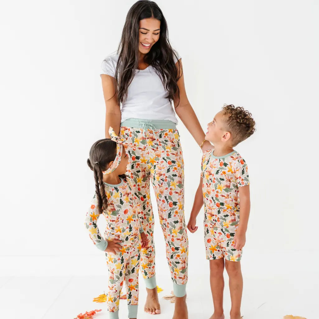 An adult in woodland print pajama pants and a white tee stands with two children in matching woodland pajamas.