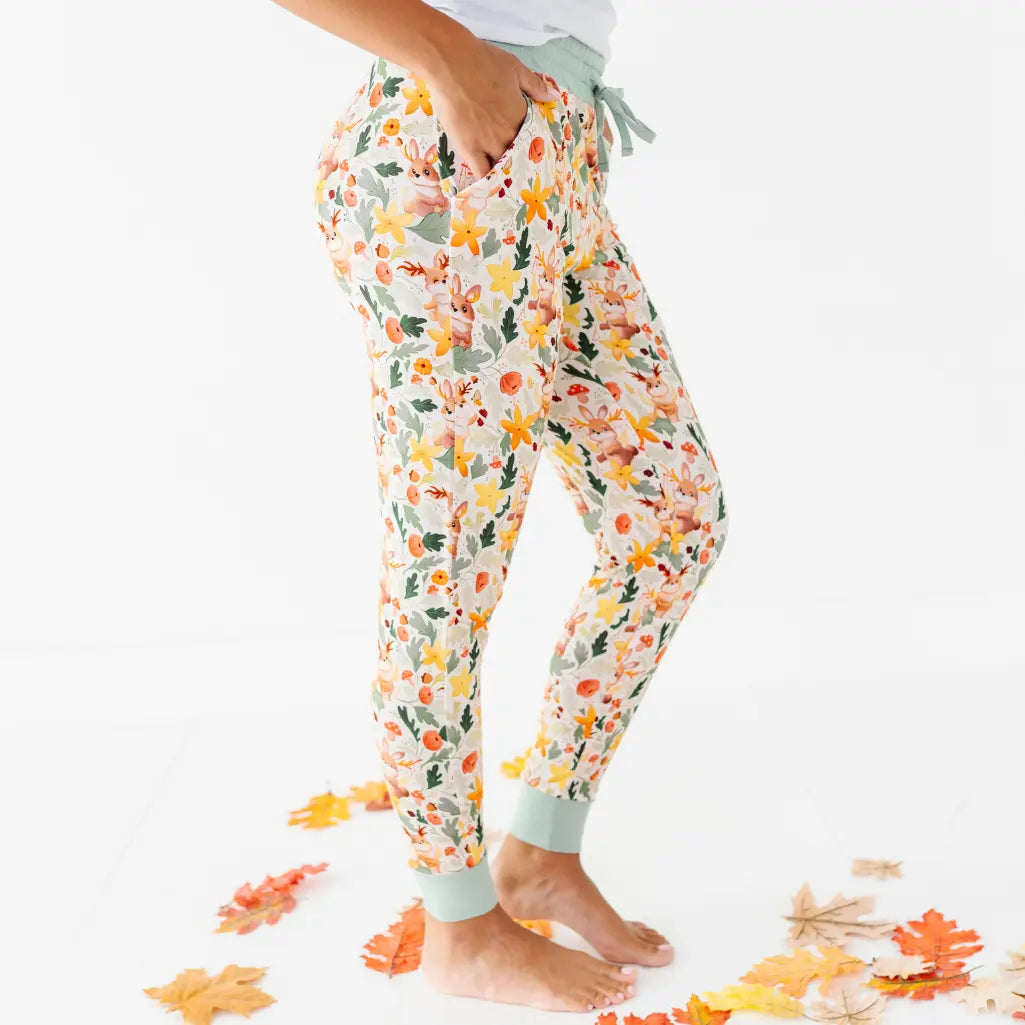 A side view of an adult with a hand in the pocket of woodland print pajama pants with sage ankle cuffs.