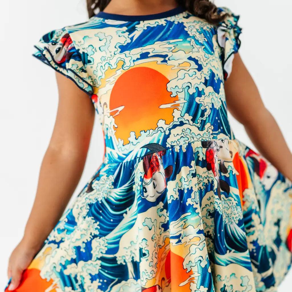 Close-up of a flutter sleeve twirl dress with navy trim showing an orange sun, cresting waves, and koi fish.