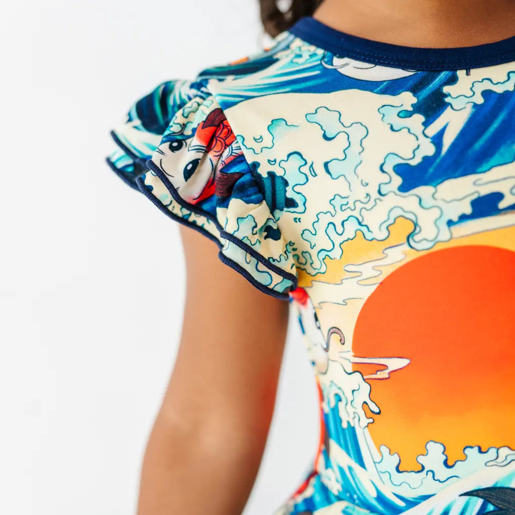 Close-up of a ruffled flutter sleeve with navy trim on a dress printed with koi fish, ocean waves, and an orange sun.