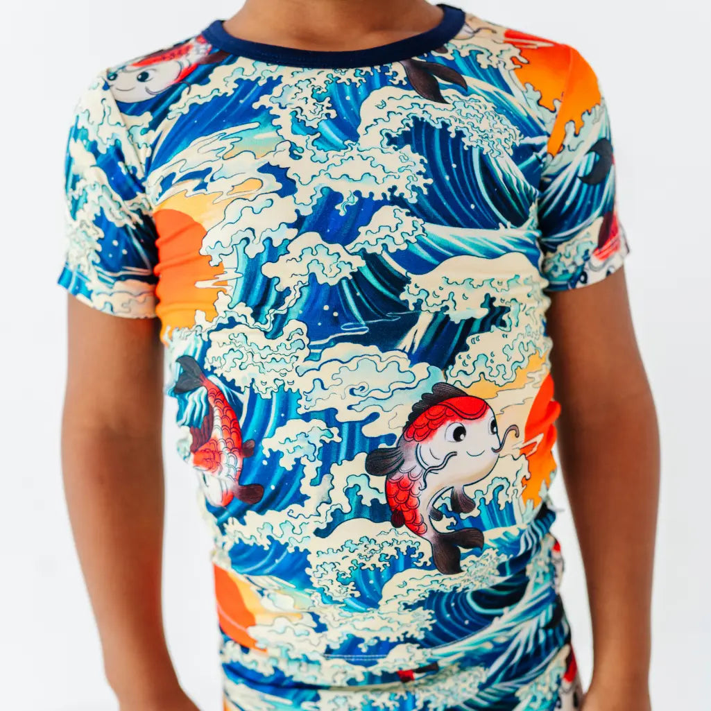 Close-up of a short sleeve pajama top with a navy collar and a print of koi fish, cresting ocean waves, and orange suns.