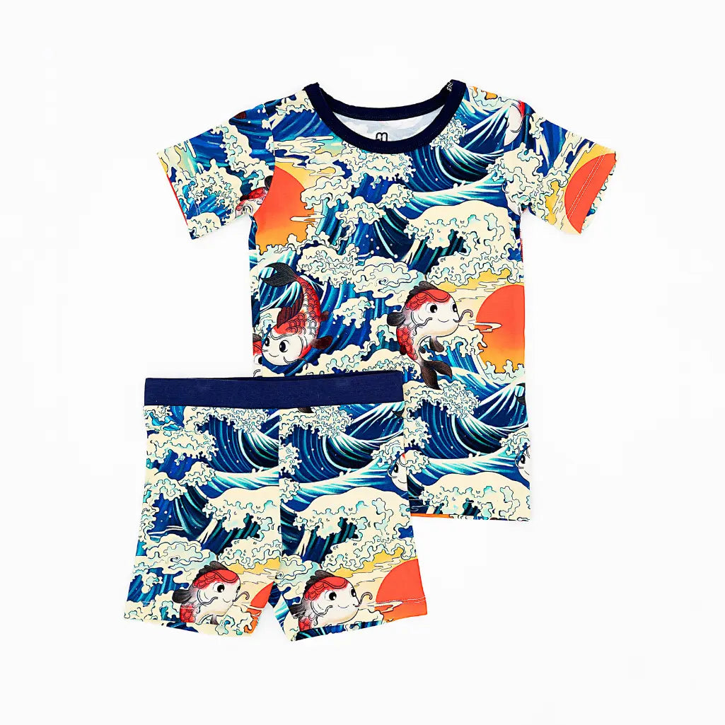 Flat lay of a short sleeve top and shorts pajama set with navy trim in a koi fish, ocean wave, and sunset print on a white background.