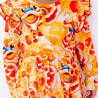 Close up of the front of a long sleeve twirl dress with flutter ruffles at the shoulders in a golden yellow print of lion dance heads and red lanterns.