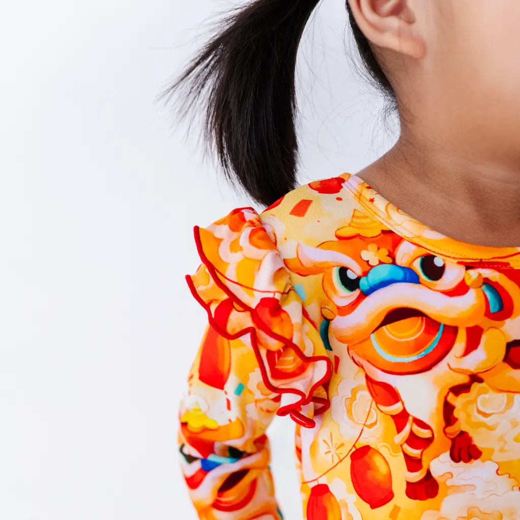 Close up of a flutter ruffle on the shoulder of a long sleeve twirl dress in a golden yellow print of lion dance heads and red lanterns.