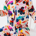 Close-up of a baby wearing a cream zip-up pajama with a colorful monster truck print and words like Go and Speed.