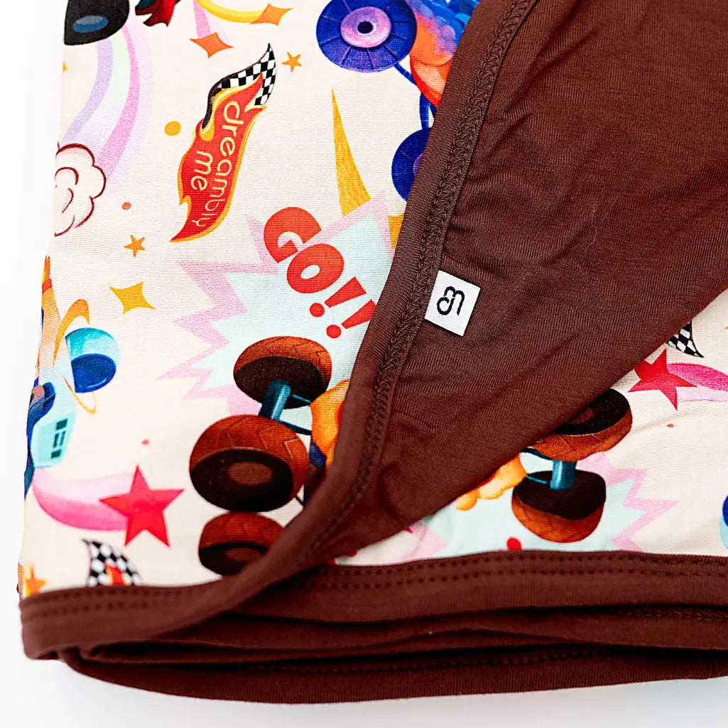 Close-up of a folded double-layered blanket with a monster truck print on one side and solid brown on the other.
