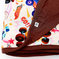 Close-up of a folded double-layered blanket with a monster truck print on one side and solid brown on the other.