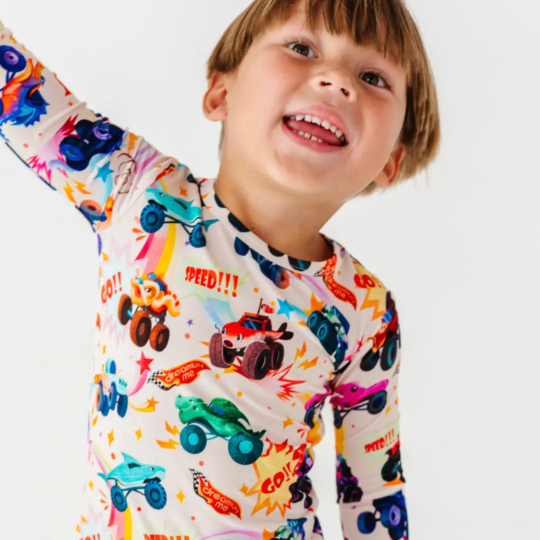 A child laughing with one arm raised, wearing a cream pajama top with a colorful monster truck print.