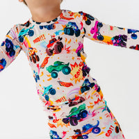 Close-up of a child in motion wearing a cream pajama set with a colorful monster truck print and words like Speed and Go.