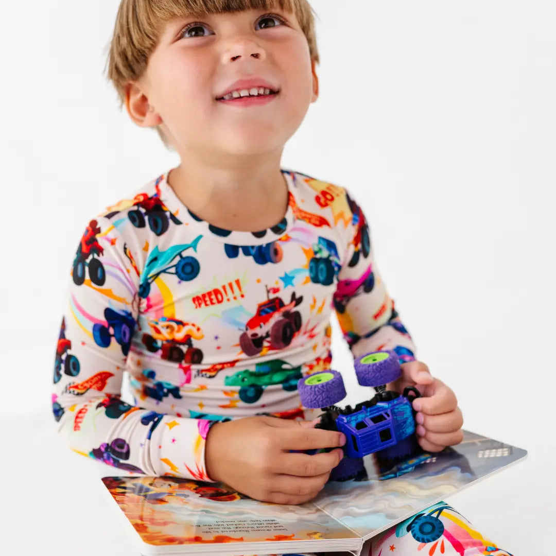 A child in monster truck print pajamas holding a toy monster truck over an open picture book.