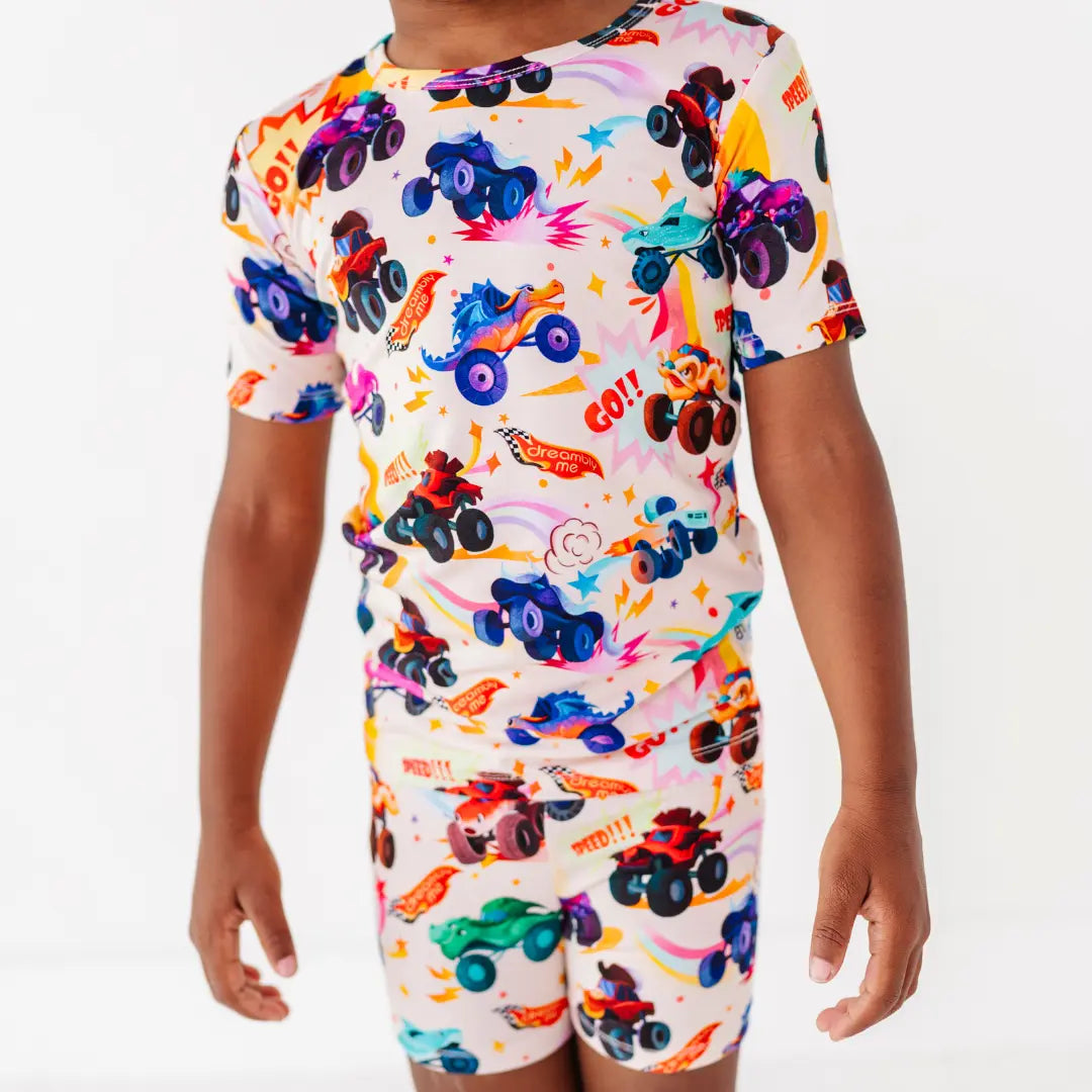 Close-up of a cream short-sleeve pajama set with a colorful monster truck print and words like Go and Speed.