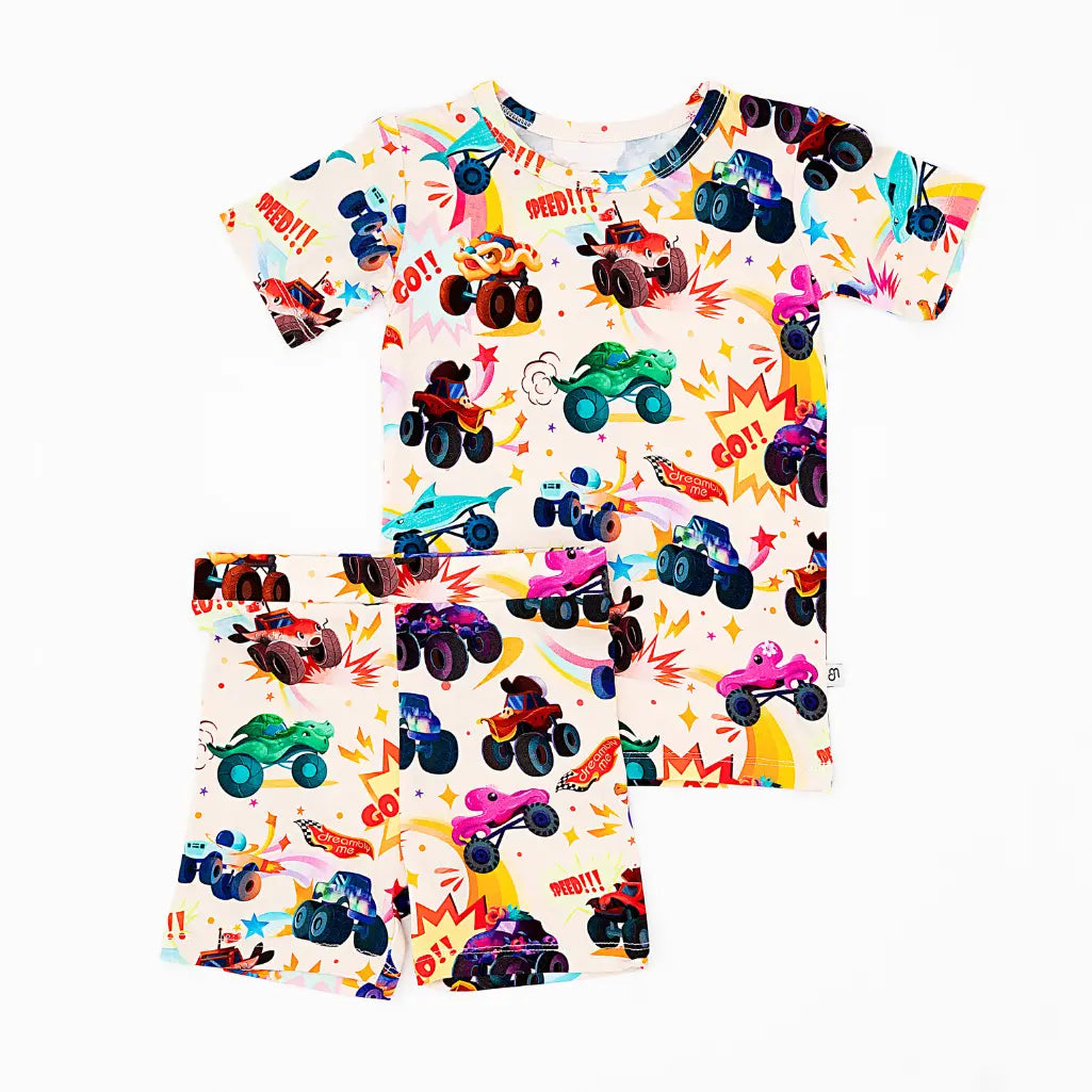 Flat lay of a cream short-sleeve top and shorts pajama set with a colorful monster truck print on a white background.
