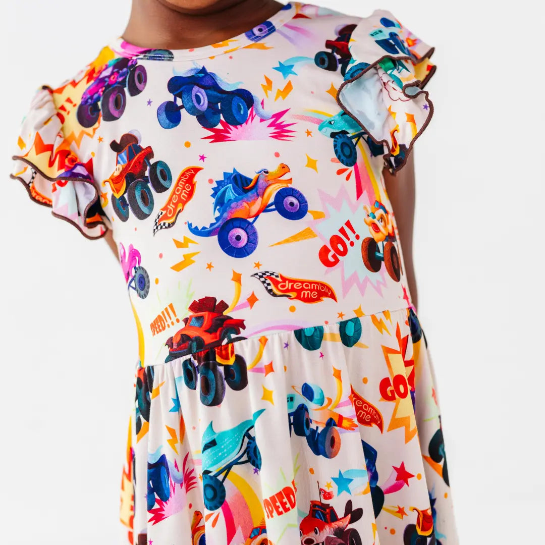 Close-up of a cream flutter-sleeve twirl dress with ruffled sleeves and a colorful monster truck print with Go and Speed lettering.