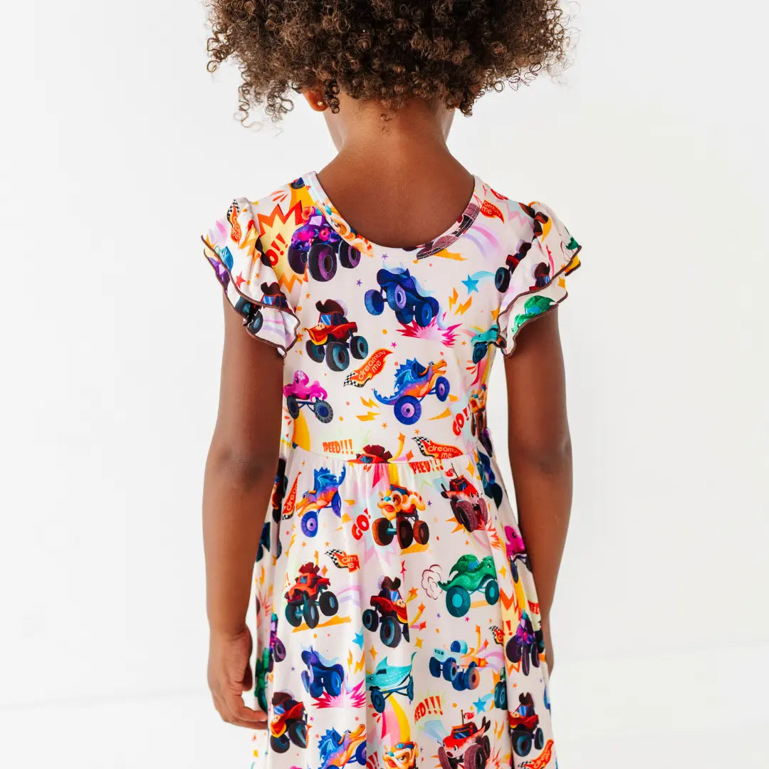 Back view of a child wearing a cream flutter-sleeve twirl dress with a colorful monster truck print.