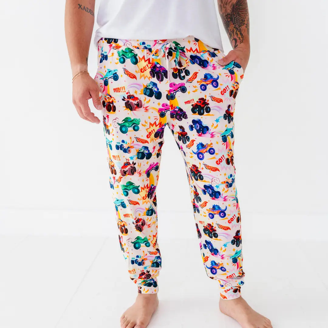 Front view of men's jogger-style pajama pants with a colorful monster truck print, one hand in the pocket.