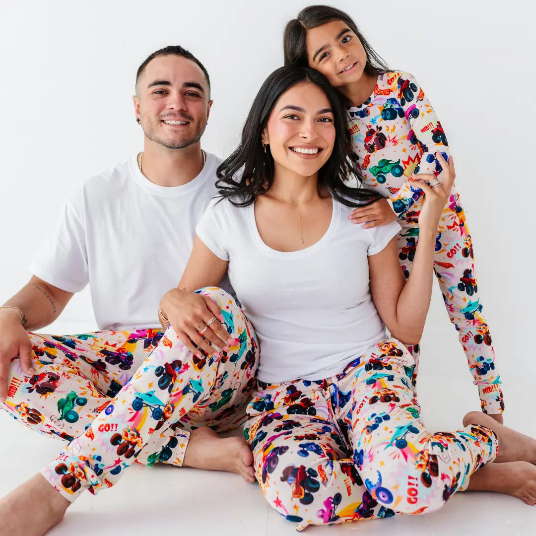 A family seated together wearing white tops and matching pajama pants with a colorful monster truck print.
