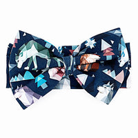 Flat lay of a large fabric bow headband in a navy geometric wolf print with triangle pine trees and snowflakes on a white background.