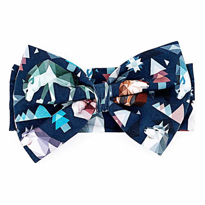 Flat lay of a large fabric bow headband in a navy geometric wolf print with triangle pine trees and snowflakes on a white background.