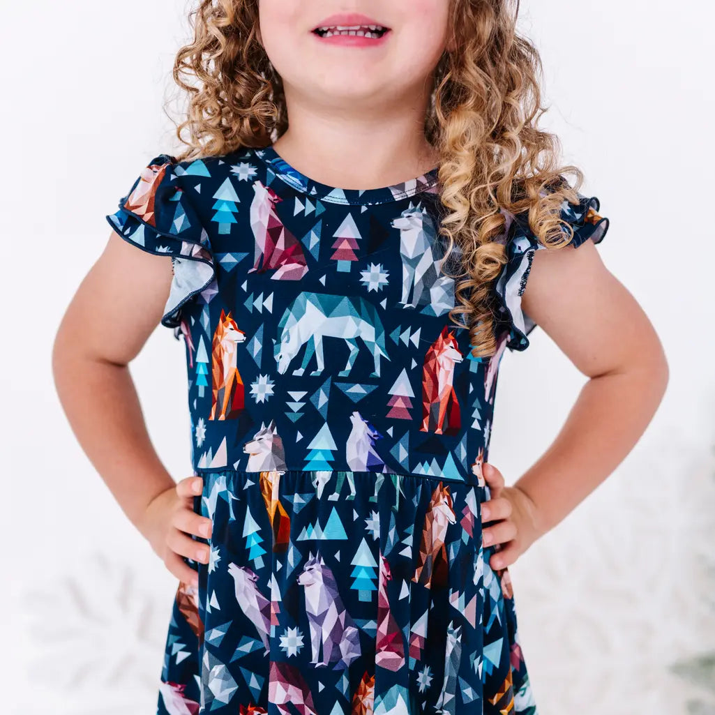 Close up of a child with both hands on the hips, showing the bodice and flutter sleeves of a twirl dress in a navy print of geometric wolves, triangle pine trees, and snowflakes.