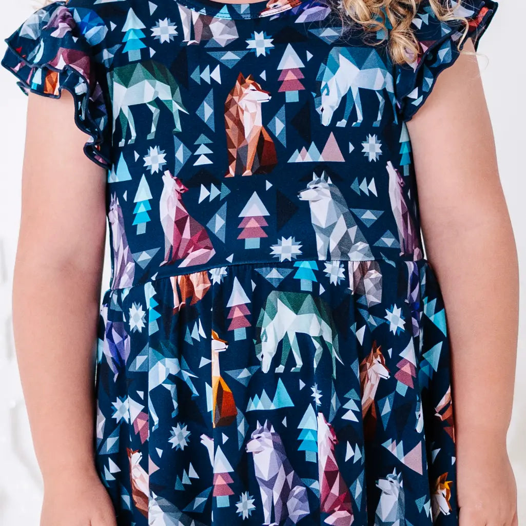Close up of the front of a flutter sleeve twirl dress with the bodice and both sleeves in a navy print of geometric wolves, triangle pine trees, and snowflakes.
