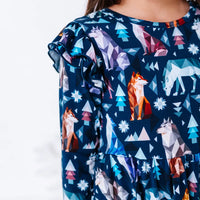 Close up of a flutter ruffle on the shoulder and the bodice of a long sleeve twirl dress in a navy print of geometric wolves, triangle pine trees, and snowflakes.