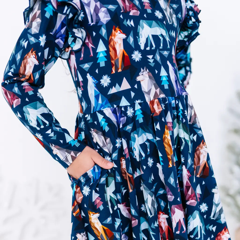Close up of a long sleeve twirl dress with a hand in the side pocket, in a navy print of geometric wolves, triangle pine trees, and snowflakes.