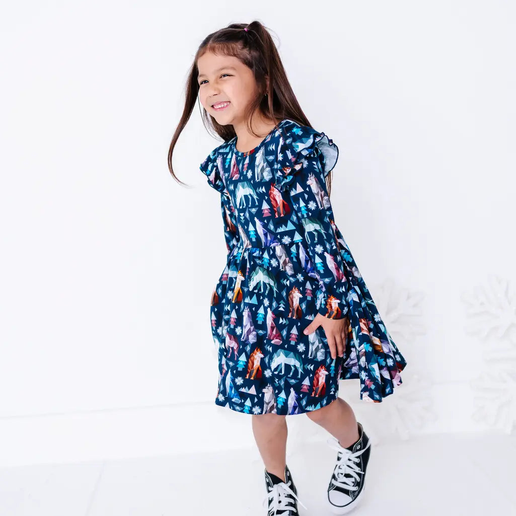 A child walking with a big smile and the skirt swinging, in a long sleeve twirl dress in a navy print of geometric wolves, triangle pine trees, and snowflakes.