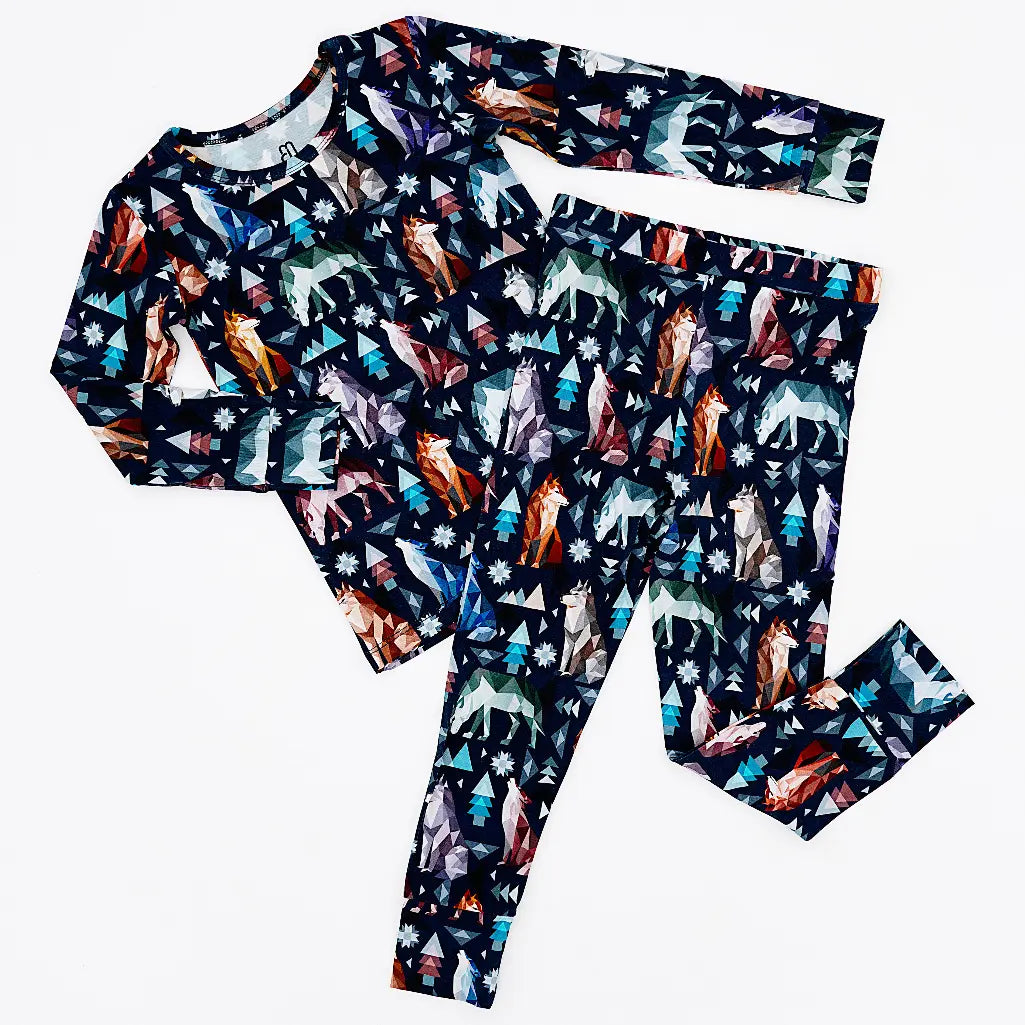 Flat lay of a long sleeve pajama top and matching pants in a navy print of geometric wolves, triangle pine trees, and snowflakes on a white background.