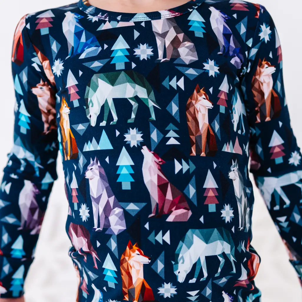 Close up of the front of a long sleeve pajama top with a round collar in a navy print of geometric wolves, triangle pine trees, and snowflakes.