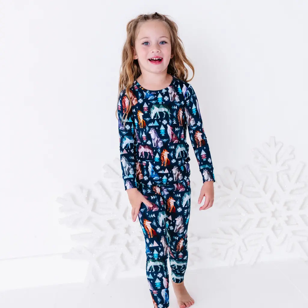 A child walking toward the camera and laughing, in a long sleeve pajama top and matching pants in a navy print of geometric wolves, triangle pine trees, and snowflakes.