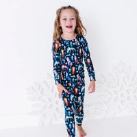 A child walking toward the camera and laughing, in a long sleeve pajama top and matching pants in a navy print of geometric wolves, triangle pine trees, and snowflakes.