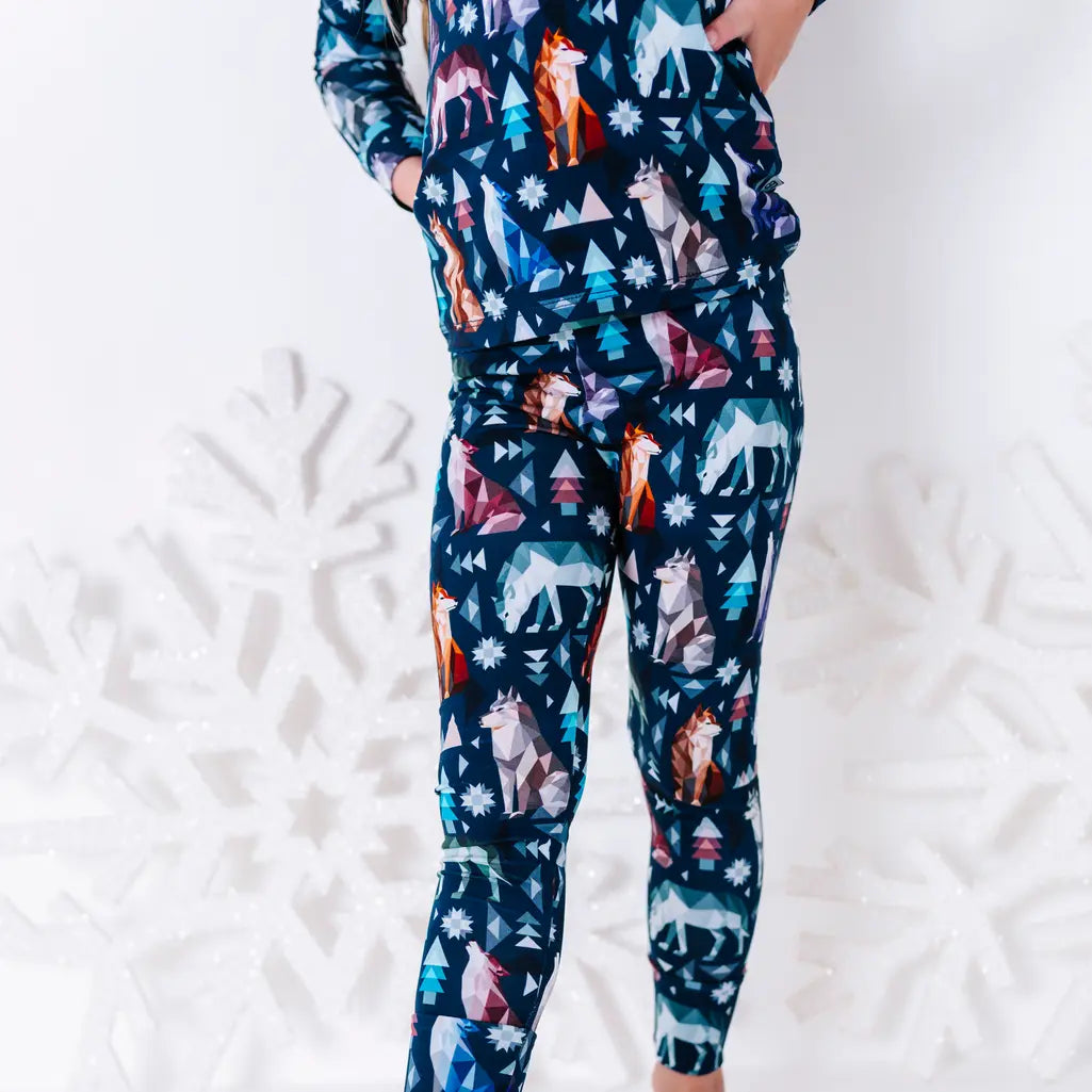 Close up of the matching pants and the hem of a long sleeve pajama top in a navy print of geometric wolves, triangle pine trees, and snowflakes.