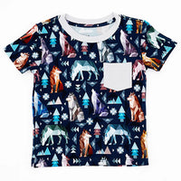 Flat lay of a short sleeve pocket tee with a cream ribbed collar and pocket in a navy print of geometric wolves, triangle pine trees, and snowflakes on a white background.