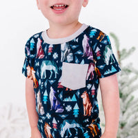 Close up of a child smiling in a short sleeve pocket tee with a cream ribbed collar and pocket in a navy print of geometric wolves, triangle pine trees, and snowflakes.
