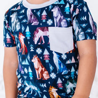 Close up of the front of a short sleeve pocket tee with a cream ribbed collar and pocket in a navy print of geometric wolves, triangle pine trees, and snowflakes.
