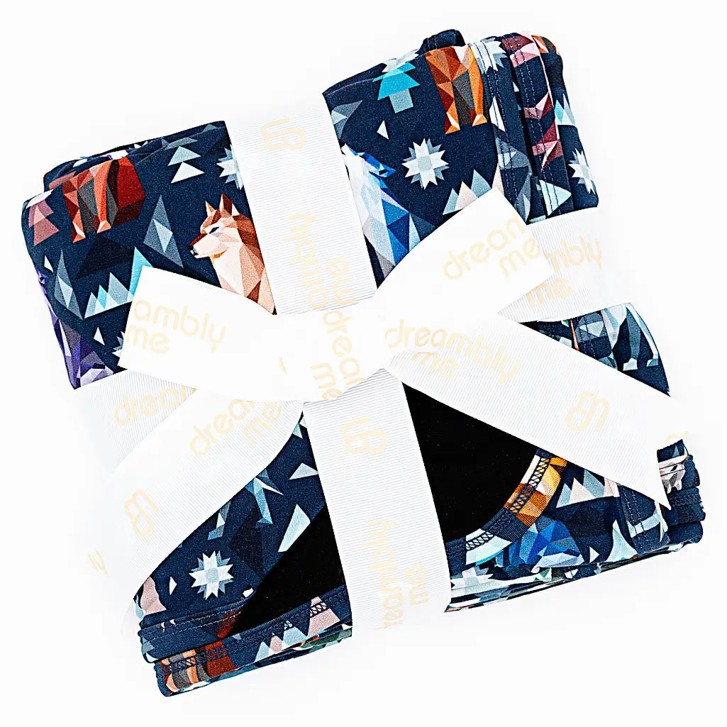 Flat lay of a folded navy blanket tied with a white ribbon in a geometric wolf print with triangle pine trees and snowflakes on a white background.