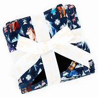 Flat lay of a folded navy blanket tied with a white ribbon in a geometric wolf print with triangle pine trees and snowflakes on a white background.
