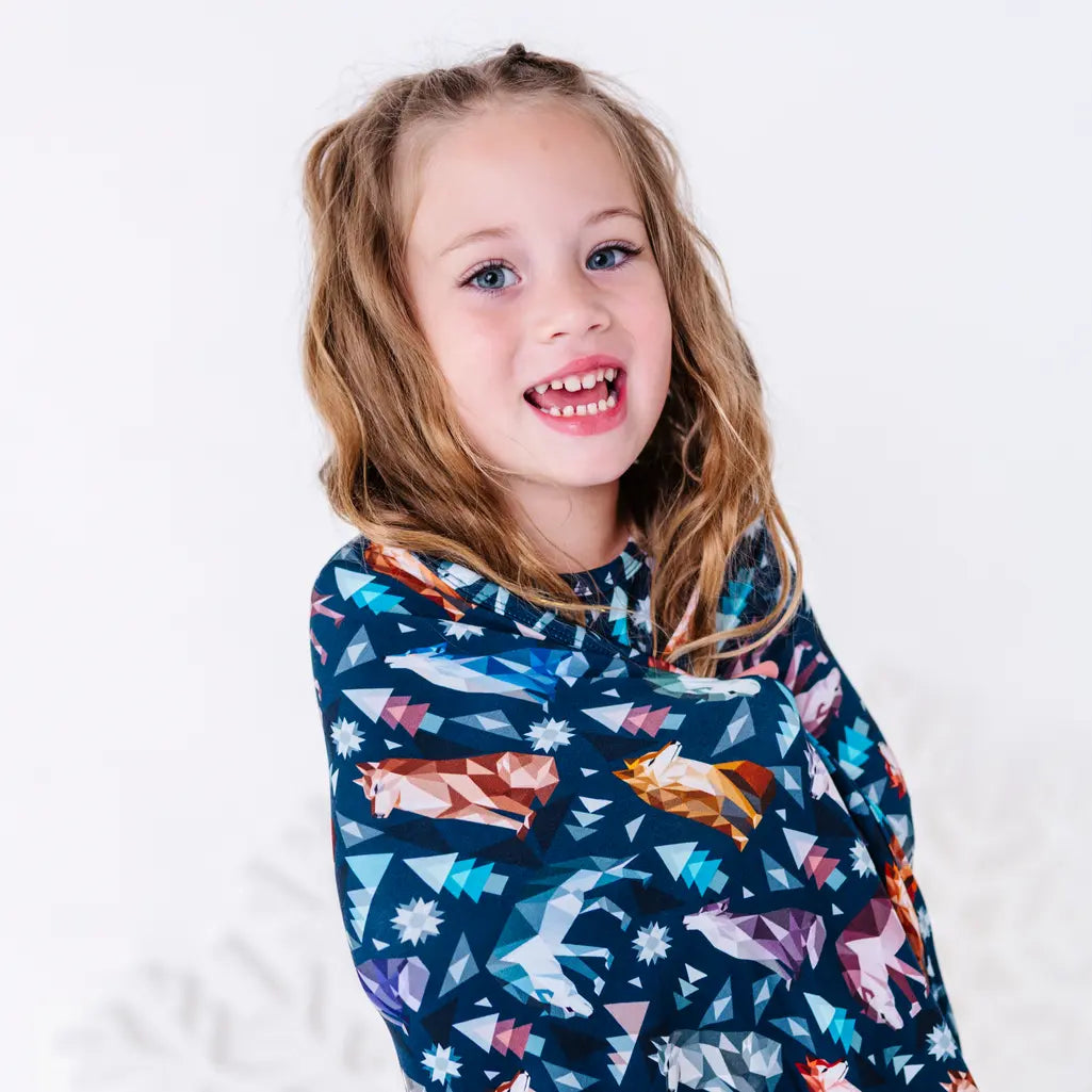 Close up of a child with a big smile wrapped in a navy blanket in a geometric wolf print with triangle pine trees and snowflakes.