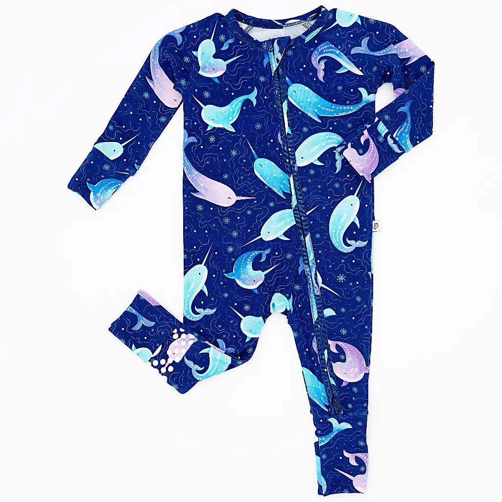 Flat lay of a zip up convertible baby pajama in a royal blue print of blue and lavender narwhals on a white background.