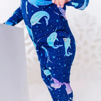 Close up of the side and leg of a zip up baby pajama in a royal blue print of blue and lavender narwhals.