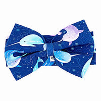 Flat lay of a large fabric bow headband in a royal blue print of blue and lavender narwhals on a white background.