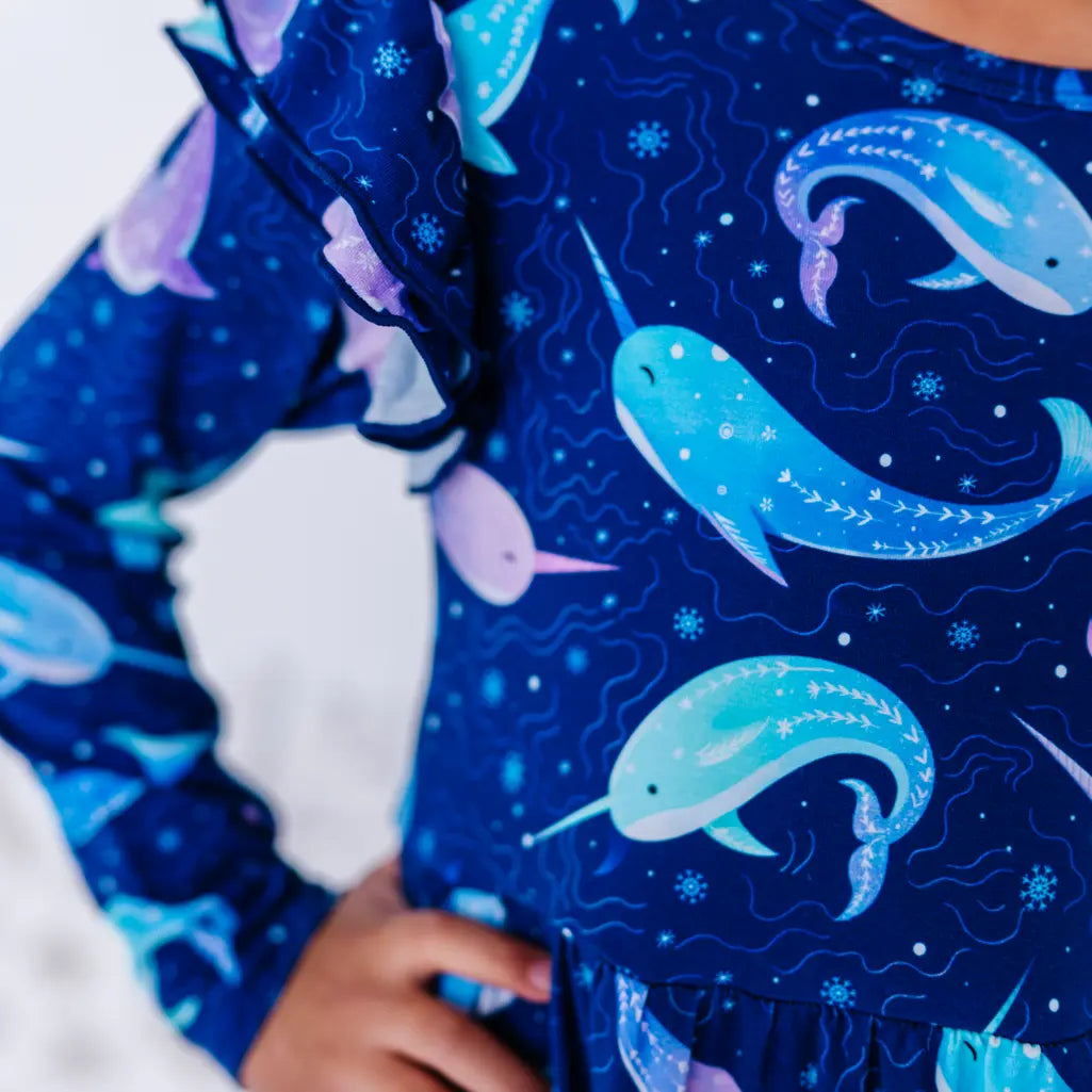 Close up of a flutter ruffle on the shoulder of a long sleeve twirl dress, showing the royal blue print of blue and lavender narwhals.